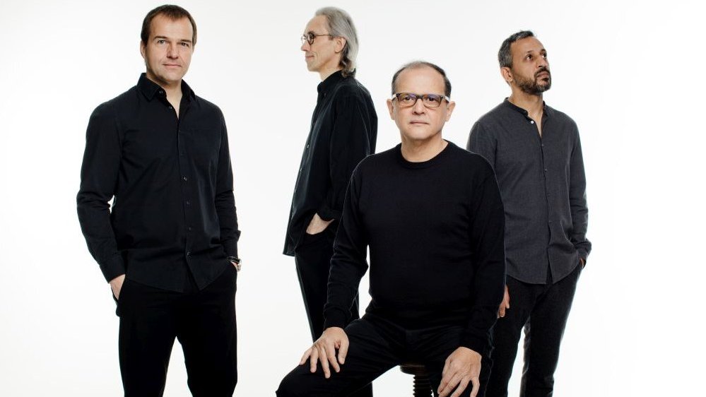 Photo of the band - four men dressed black, each of them looking in different direction, on white background