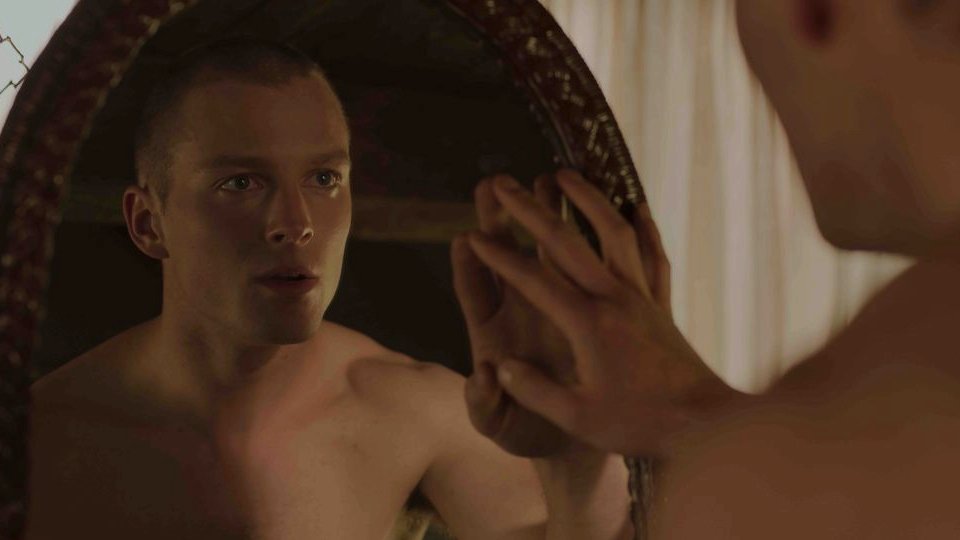 Photo from the movie: a young undressed man looking at the mirror on his reflection and touching the mirror with his right hand