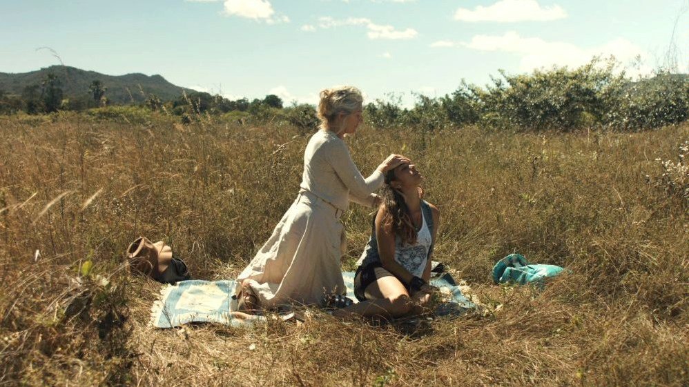 Photo from the movie: two women sitting on a blanket on a field covered with grass and bushes.
