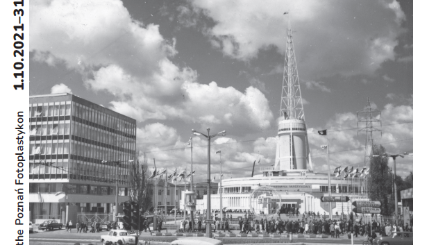 Black and white photo of a fair spire - a symbol of Poznań fair. In the foreground - a street, people waiting at the zebra crosing and a delivery car.