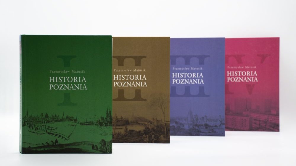 Cztery tomy książki w kolorach, od lewej: zielonym, brązowym, niebieskim i czerwonym.