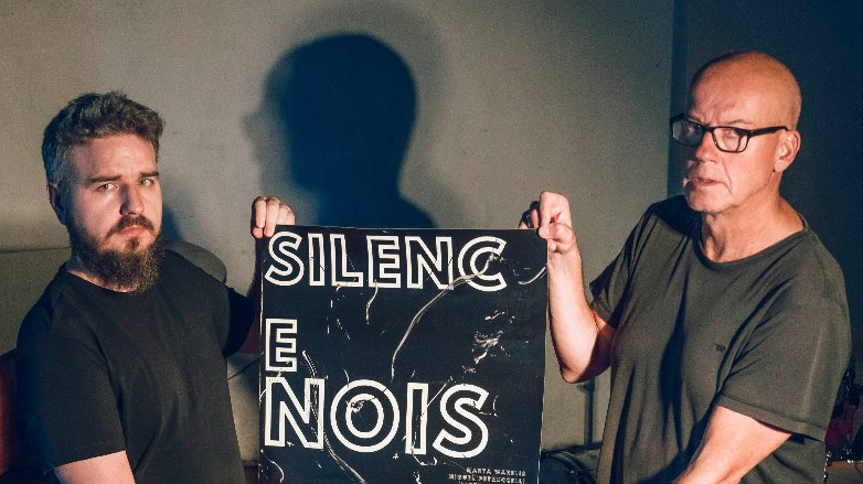 Dwóch mężczyzn trzyma plakat reklamujący festiwal z napisem "Silence. Noise".