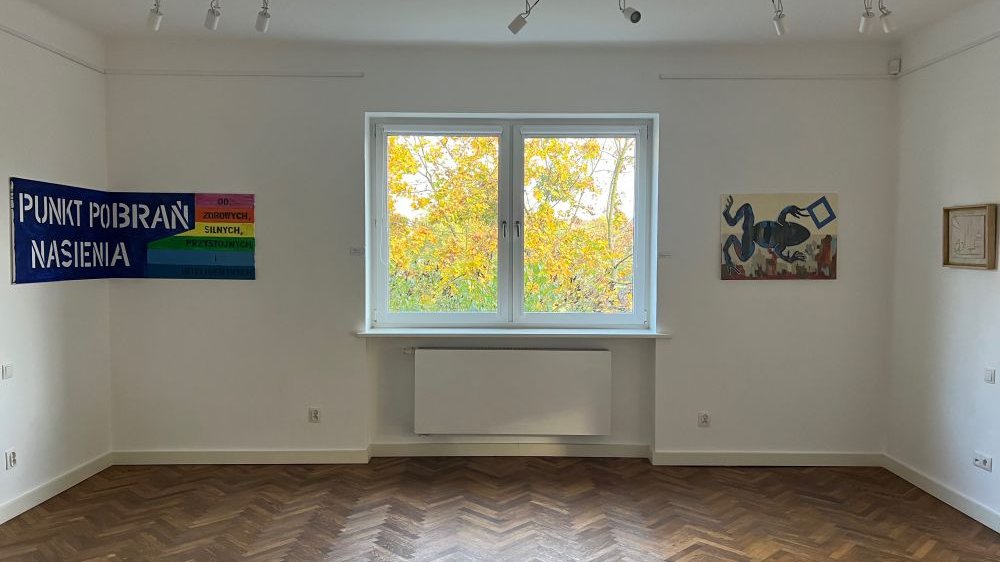 Pomieszczenie w Galerii Ego, na ścianach wiszą prace, a w oknie widać drzewo o żółknących liściach.