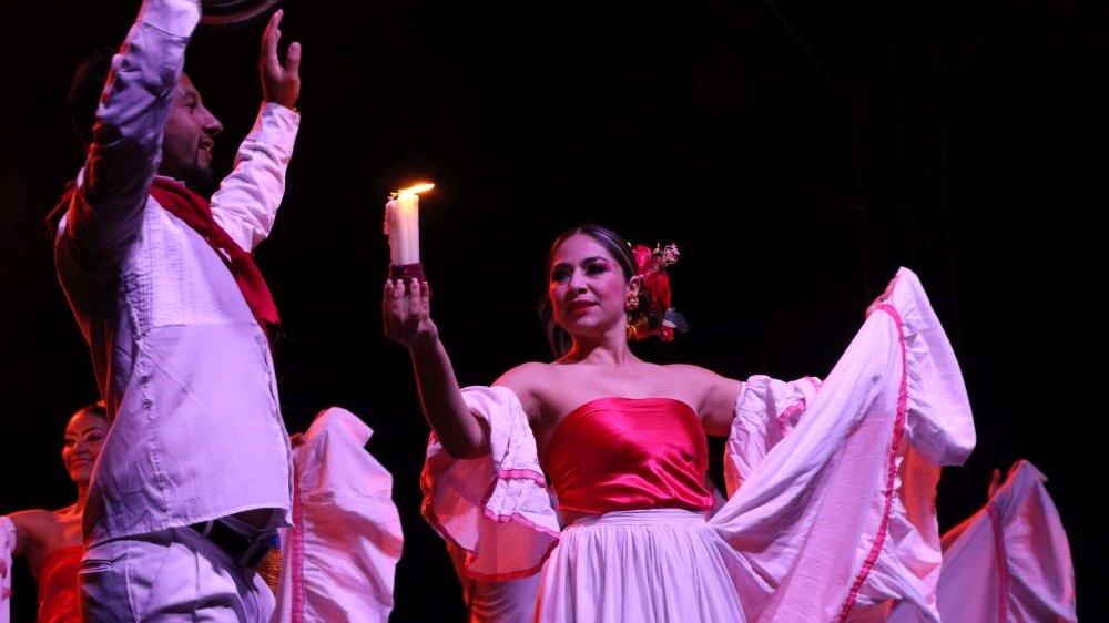 Tancerka w czerwono-białej, falbaniastej sukni trzyma w jednej ręce zapaloną świeczkę, a w drugiej rąbek sukni. Zbliża się do tancerza w białym kostiumie.