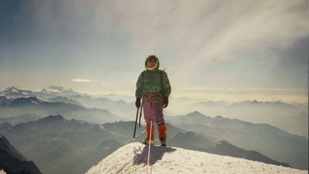 Mężczyzna w zimowym stroju pozuje na zdobytym szczycie góry.