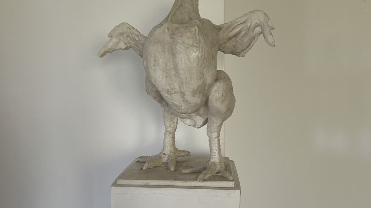 Szara rzeźba przedstawia dziwne stworzenie, najpewniej jest to hybryda kury i orła.