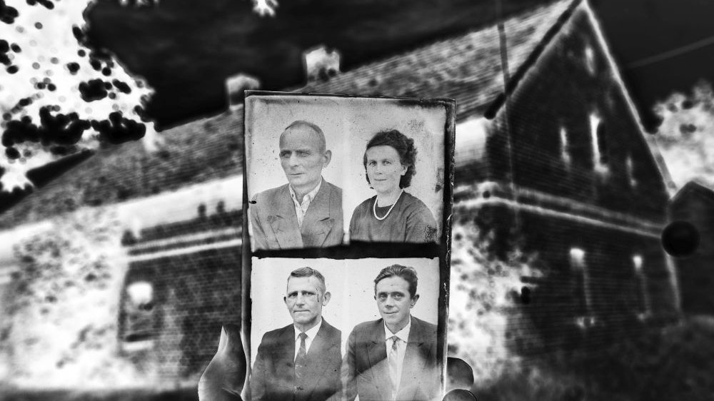 Czarno-białe zdjęcie przedstawiające trzymane w ręku portrety ludzi na tle starego domu.