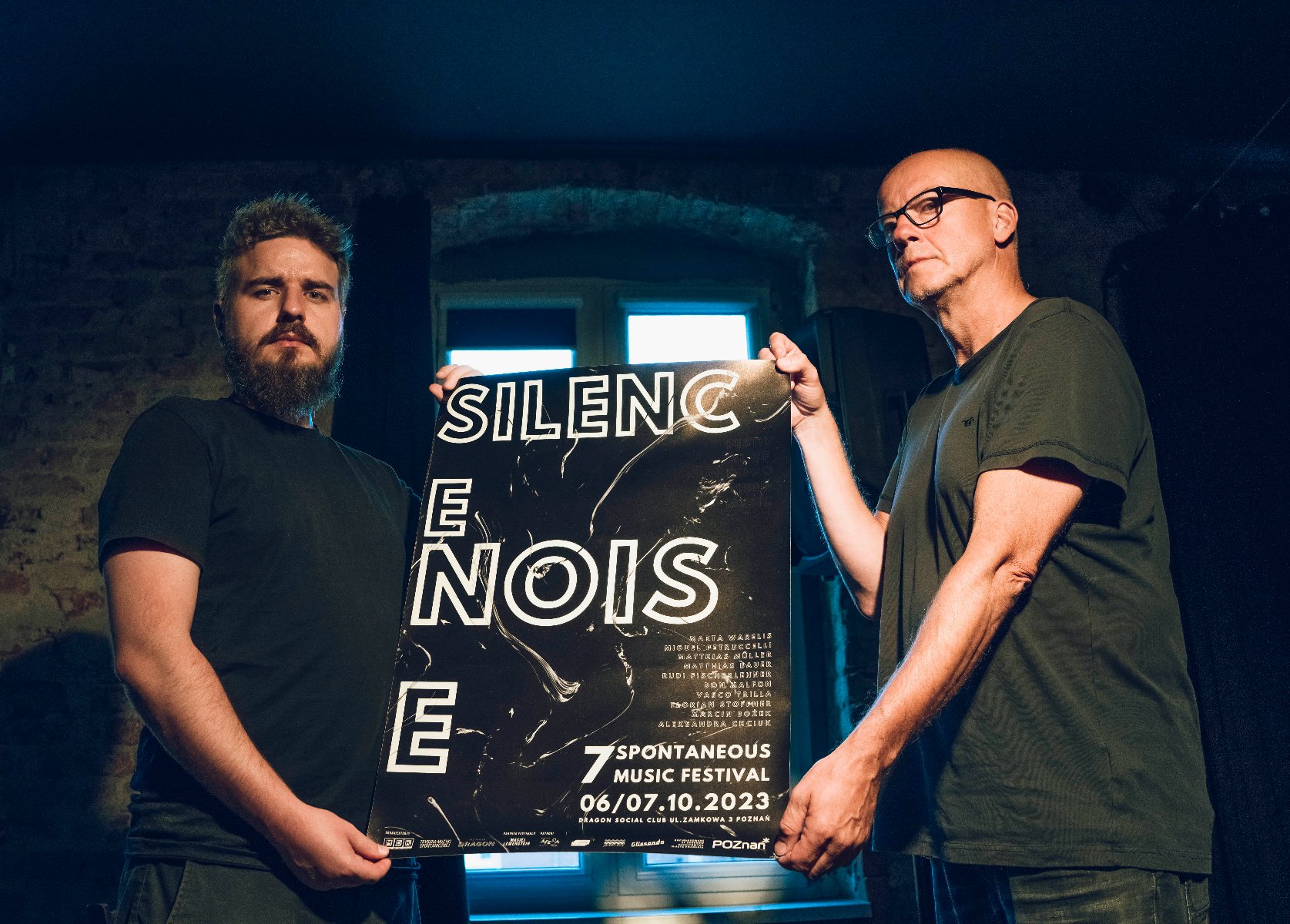Dwóch mężczyzn trzyma plakat reklamujący festiwal z napisem "Silence. Noise". - grafika artykułu