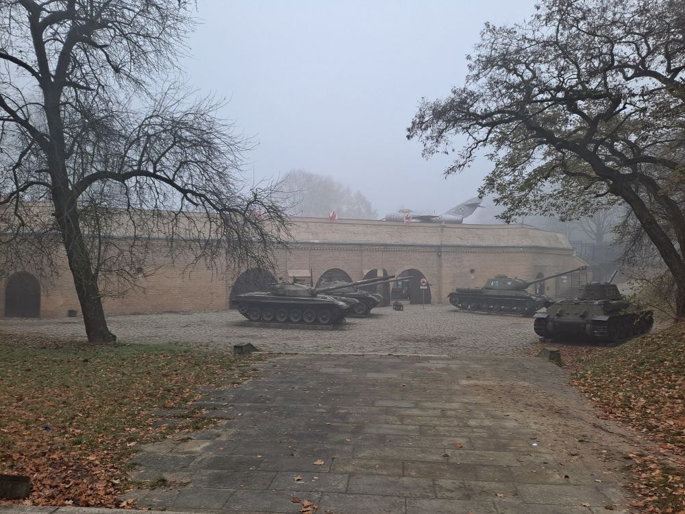 Mglisty jesienny dzień, w oddali widać zabytkowe czołgi, za nimi ceglany mur. - grafika artykułu