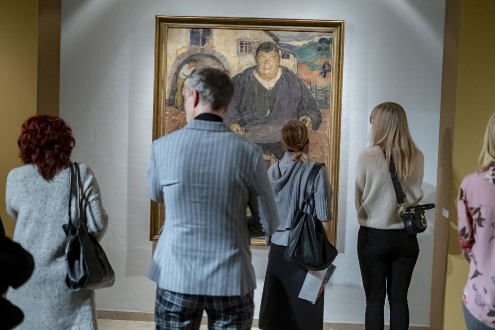 Ludzie na wystawie oglądają obraz przedstawiający mężczyznę, stoją tyłem do obiektywu. - grafika artykułu