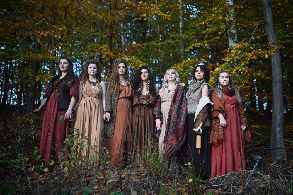 Siedem kobiet w długich włosach i sukniach stoi w lesie. - grafika artykułu