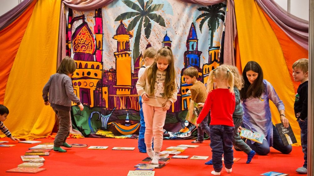 Dzieci bawią się na tle rozpiętej, kolorowej tkaniny, na której namalowano bajkowy zamek.