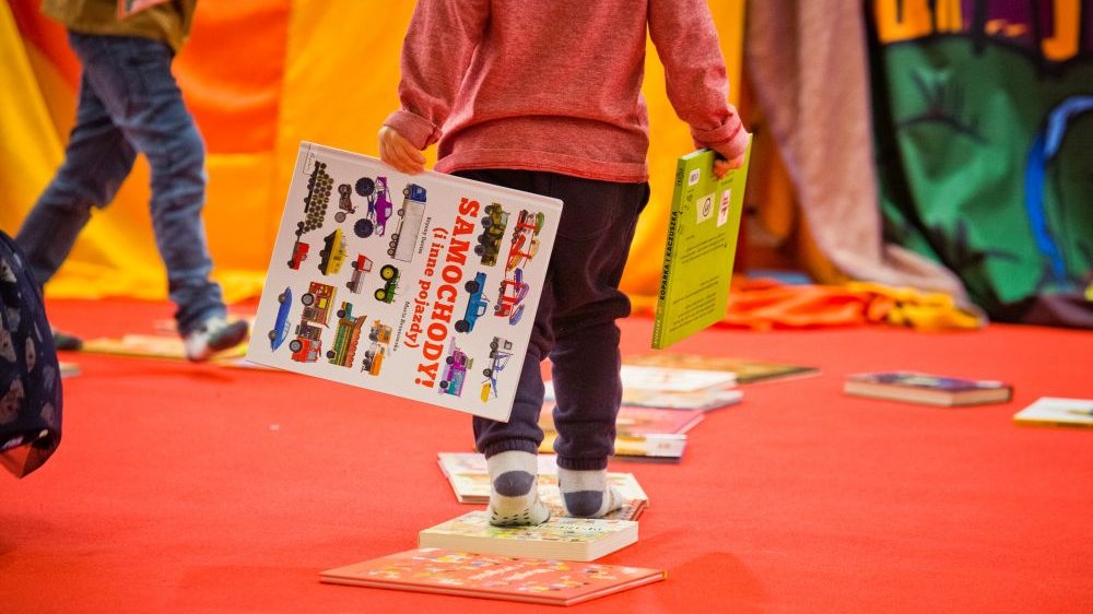 Widoczne od pasa w dół dziecko idące z dwiema kolorowymi książkami w rękach.